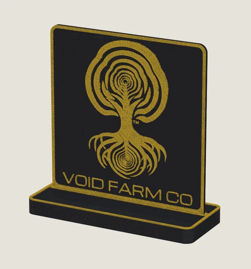Black desk sign with the Void Farm Co tree-and-roots logo in gold, framed by a raised gold rim that holds resin fill, in a matching stand.